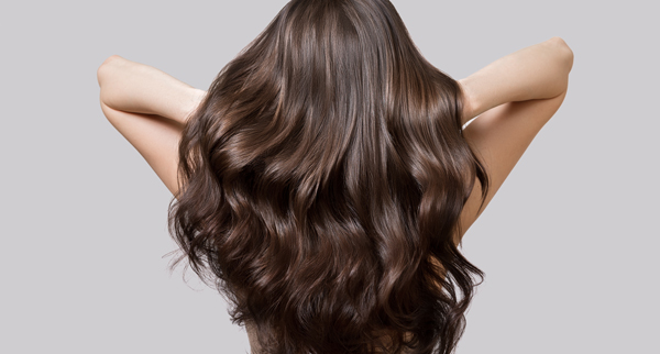 brunette hair flowing in waves with hands behind head showing healthy hair shine and volume