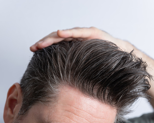 man styling his hair with gray highlights showing modern hairstyle trends