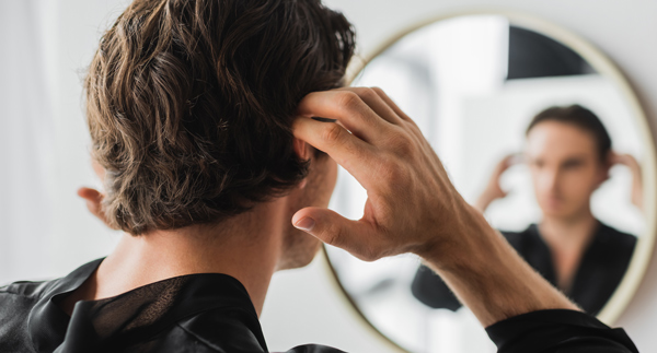 man adjusting hair in front of mirror reflecting stylish grooming
