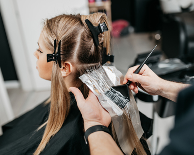 woman getting hair colored at salon with foil and brush for highlights