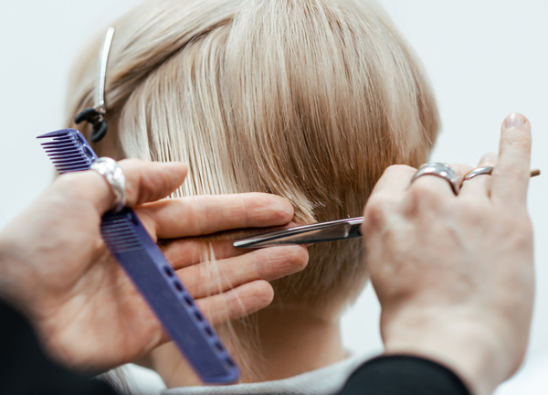 a hairstylist cutting short blonde hair using scissors and a comb demonstrating a professional haircut technique