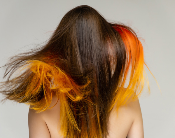woman with long hair in motion displaying vibrant orange and yellow highlights capturing the essence of hairstyle trends