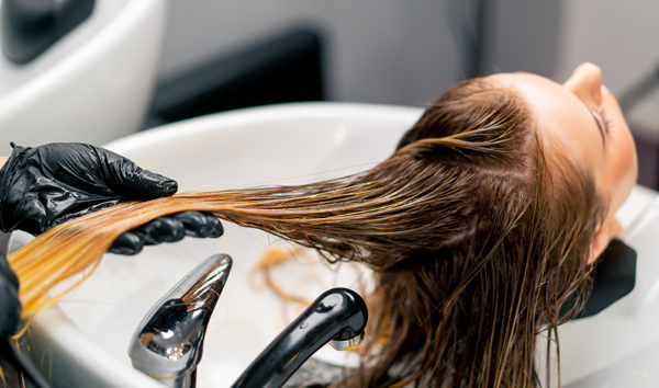 person receiving a hair treatment at a salon with a stylist applying product to long hair emphasizing healthy shiny strands during a relaxing experience