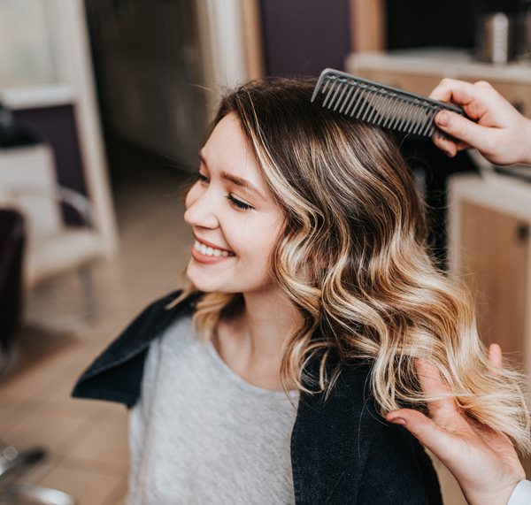 smiling woman getting hair styled in salon with hair comb