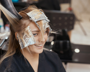 smiling woman in salon with foil hair highlights getting haircut and styling treatment