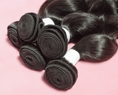 four bundles of smooth black hair extensions on a pink background