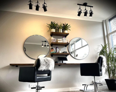 modern salon interior with two circular mirrors stylish black chairs and floating shelves with plants and beauty products