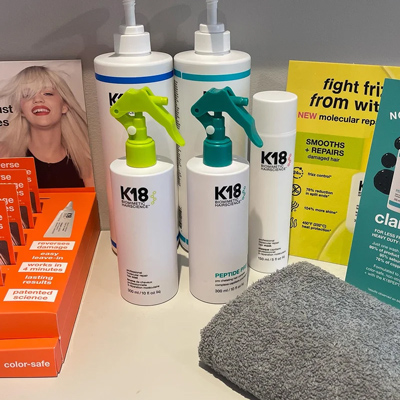bottles of K18 hair treatment products on a display with a gray towel and promotional materials designed for damaged hair repair and enhancement